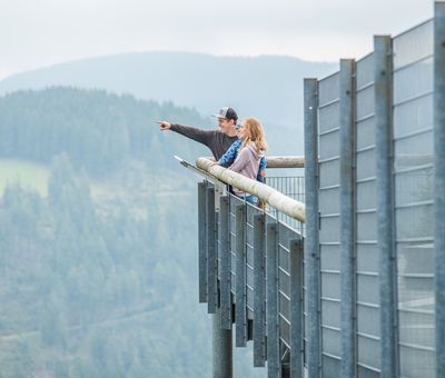Ein Paar steht gemeinsam auf der Panorama Erlebnis Brücke und schaut und zeigt in die Ferne