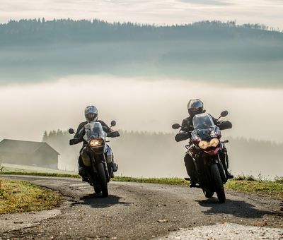 Zwei Motorradfahrer vor bergiger Landschaft im Nebel