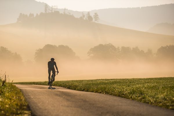 Biker fährt eine asphaltierte Straße hoch, die Landschaft ist mit Nebel bedeckt